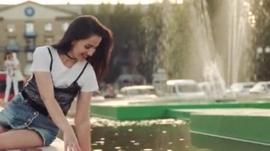 Denim şort genç kadın nazlanma bir şehir çeşme su içinde sıçramaları yapma oynar.