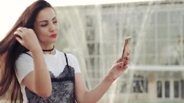 Mladá dívka narovní vlasy a dívá se na kameru smartphone. — Stock video