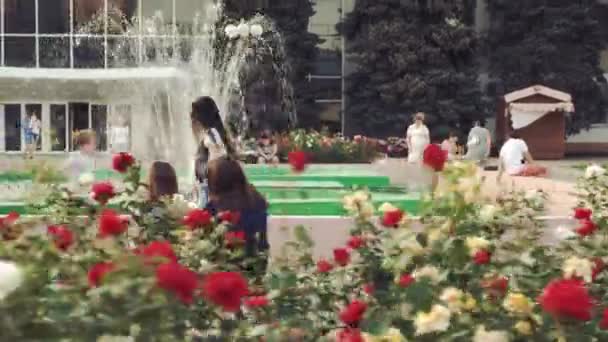 Girl lekfullt går nära stadens fontän och rabatter med rosor — Stockvideo