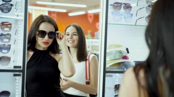 Vriendinnen kiezen zonnebril, proberen op hen in de voorkant van de spiegel. — Stockvideo