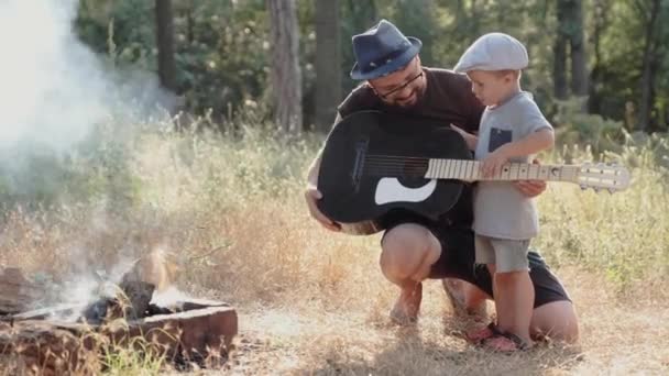 Far och hans lille son med gitarr med picknick i skogen — Stockvideo