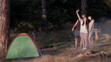 Çadırve kamp ateşinin yakınındaki ormanda bir grup genç, telefonlarının kamerasıyla selfie çekti..