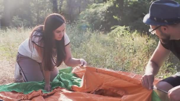 Jeune femme caucasienne et l'homme mettre en place leur tente ensemble sur une journée d'été ensoleillée . — Video