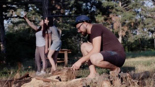 Ön planda adam yemek pişirmek için bir kamp ateşi meşgul iken iki kız bir selfie çekmek. — Stok video