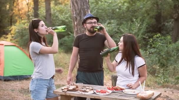 Concepto de ocio y la gente - amigos felices brindis, bebidas, fiesta de verano en el bosque con tienda al atardecer . — Vídeos de Stock