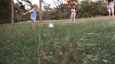 Çocuklu yetişkinler orman bahçesinde futbol oynuyor.