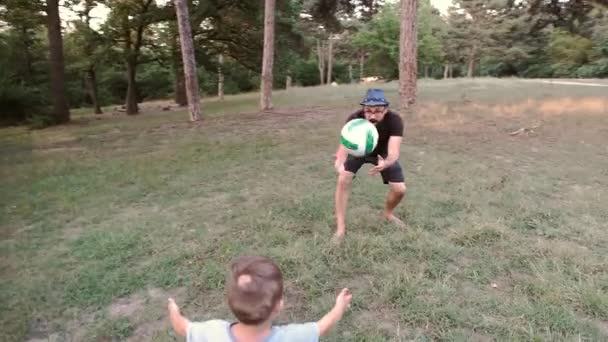 Ein Kind mit Eltern und Familienfreunden spielt einen Ball auf einer Waldlichtung. — Stockvideo