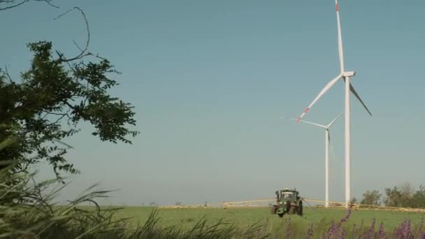 Un tractor con un dispositivo para rociar campos se encuentra entre el campo sobre el fondo de las turbinas eólicas . — Vídeo de stock