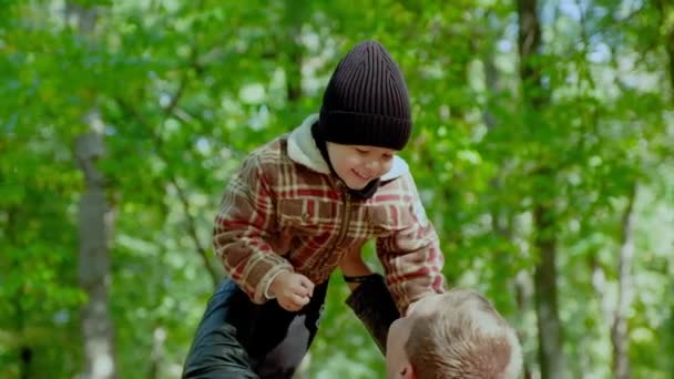 Молоді батьки грають і обіймають маленького сина в сонячному осінньому лісі — стокове відео