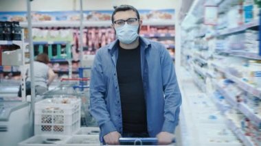Yüz maskeli ve gözlüklü adam süpermarkette yürüyor.