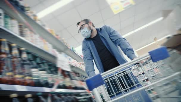 Чоловік у масці дивиться на пиво на полицях в сучасному супермаркеті — стокове відео
