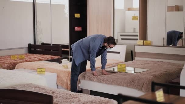 Customer in mask chooses comfortable bed in furniture store — Stock Video