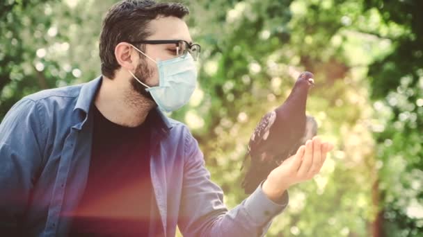 Een man met een beschermend medisch masker bewondert een duif op zijn arm.. — Stockvideo