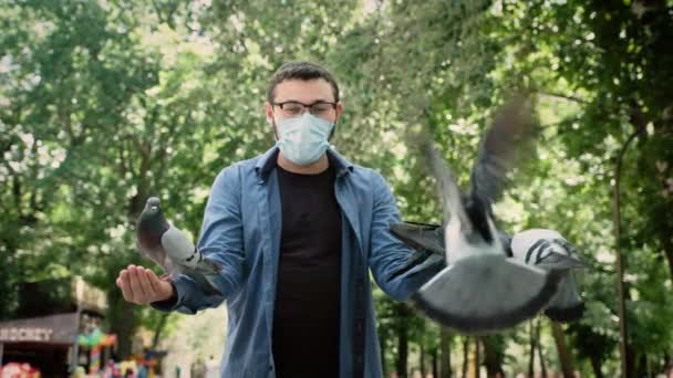 Les pigeons sont assis sur les mains d'un homme qui a un masque médical sur le visage — Video