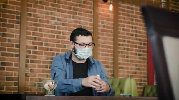 Чоловік в кафе їсть морозиво, не знімаючи маску з обличчя . — стокове відео