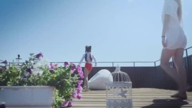 Ebeveynler plastik şezlonglara uzanır ve kızlar sandalyeye oturur.