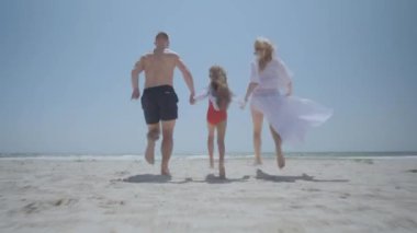 Mayolu neşeli aile sarı kumsalda koşuyor.
