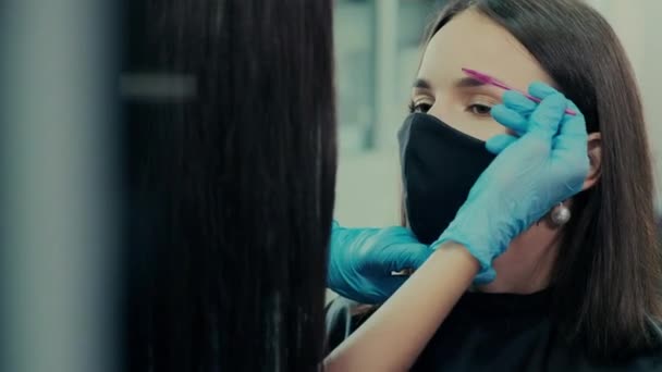 Artista en guantes pinceles cejas de cliente en máscara en salón — Vídeo de stock