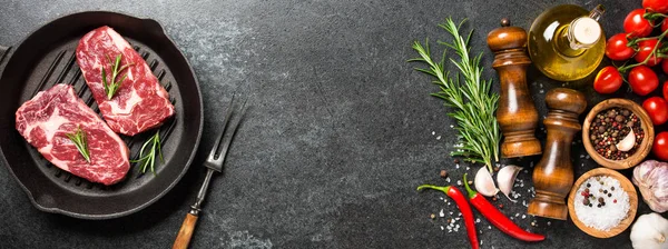 Свежие сырые стейки на сковороде и специи на черном камне — стоковое фото