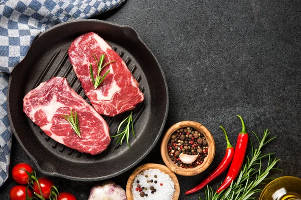 Steak iga mentah segar pada panci panggangan dan rempah-rempah di atas batu hitam — Stok Foto