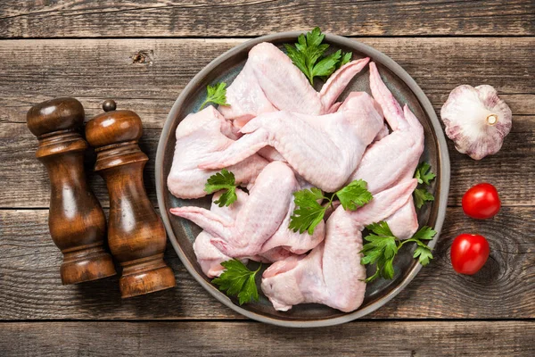Свежие сырые куриные крылышки на керамической тарелке и специи для приготовления пищи — стоковое фото