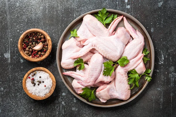 Свежие сырые куриные крылышки на керамической тарелке и специи для приготовления пищи — стоковое фото