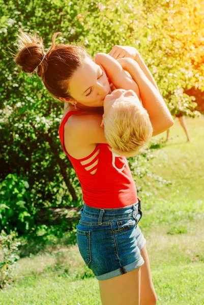 Mutlu genç esmer anne ve oğlu açık havada Park güneşli bahar gününde. Sportif Genç Anne oğlunu eğleniyor parkta kaldırma annelik keyfi.