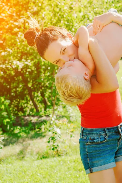 Mutlu genç esmer anne ve oğlu açık havada Park güneşli bahar gününde. Sportif Genç Anne oğlunu eğleniyor parkta kaldırma annelik keyfi.