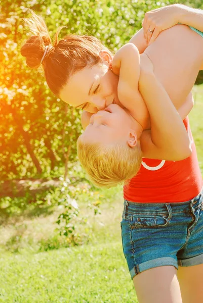 Mutlu genç esmer anne ve oğlu açık havada Park güneşli bahar gününde. Sportif Genç Anne oğlunu eğleniyor parkta kaldırma annelik keyfi.