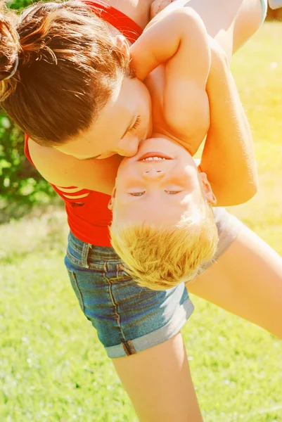 Mutlu genç esmer anne ve oğlu açık havada Park güneşli bahar gününde. Sportif Genç Anne oğlunu eğleniyor parkta kaldırma annelik keyfi.