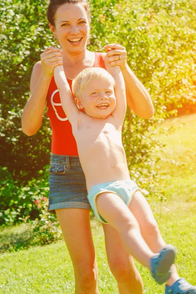 Mutlu genç esmer anne ve oğlu açık havada Park güneşli bahar gününde. Sportif Genç Anne oğlunu eğleniyor parkta kaldırma annelik keyfi.