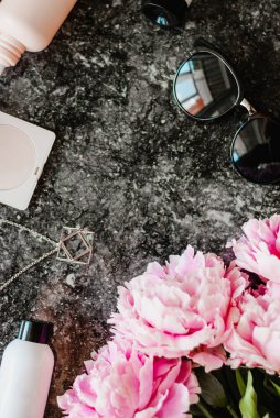 Güzellik düz aksesuarları, parfüm, kozmetik ve peonies karanlık mermer zemin üzerine yatırın. Üstten görünüm