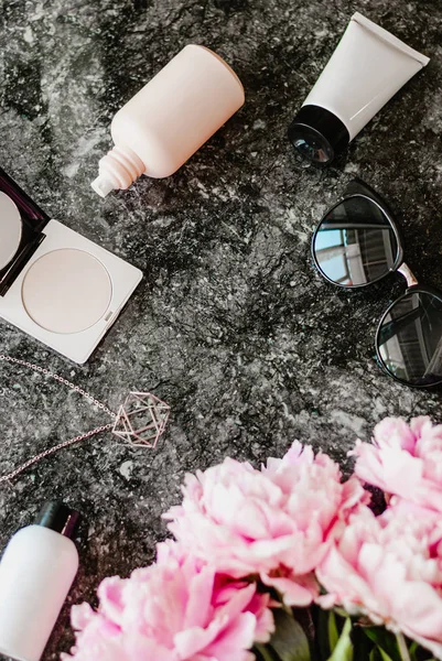 Güzellik düz aksesuarları, parfüm, kozmetik ve peonies karanlık mermer zemin üzerine yatırın. Üstten görünüm