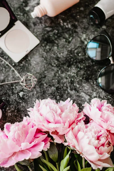 Güzellik düz aksesuarları, parfüm, kozmetik ve peonies karanlık mermer zemin üzerine yatırın. Üstten görünüm