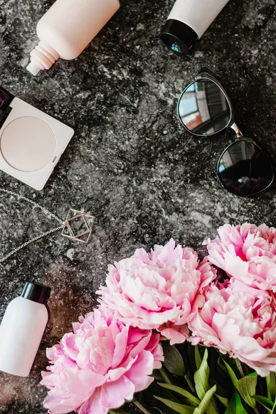 Güzellik düz aksesuarları, parfüm, kozmetik ve peonies karanlık mermer zemin üzerine yatırın. Üstten görünüm