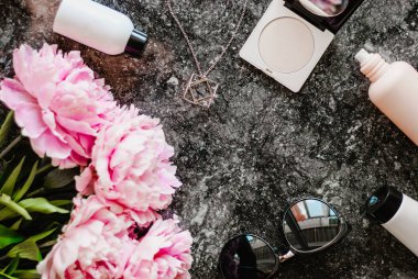 Güzellik düz aksesuarları, parfüm, kozmetik ve peonies karanlık mermer zemin üzerine yatırın. Üstten görünüm