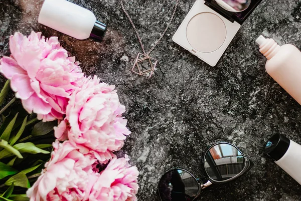 Güzellik düz aksesuarları, parfüm, kozmetik ve peonies karanlık mermer zemin üzerine yatırın. Üstten görünüm