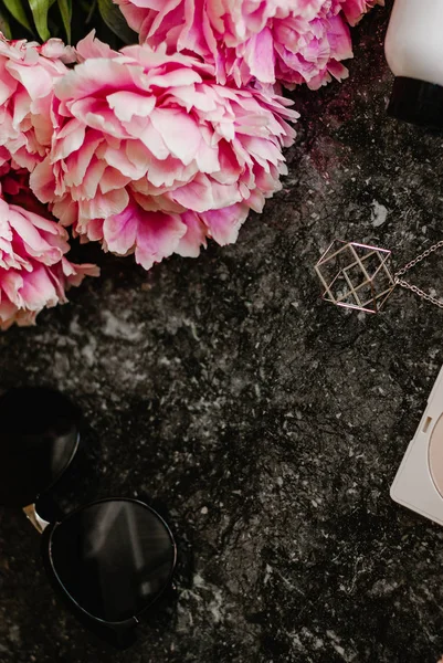 Güzellik düz aksesuarları, parfüm, kozmetik ve peonies karanlık mermer zemin üzerine yatırın. Üstten görünüm