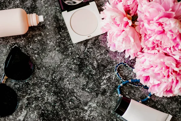 Güzellik düz aksesuarları, parfüm, kozmetik ve peonies karanlık mermer zemin üzerine yatırın. Üstten görünüm