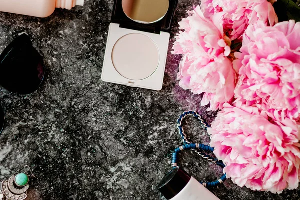 Güzellik düz aksesuarları, parfüm, kozmetik ve peonies karanlık mermer zemin üzerine yatırın. Üstten görünüm