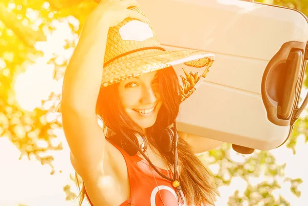 Hasır şapkalı büyük bir bavul tutan bir genç kız bir seyahate