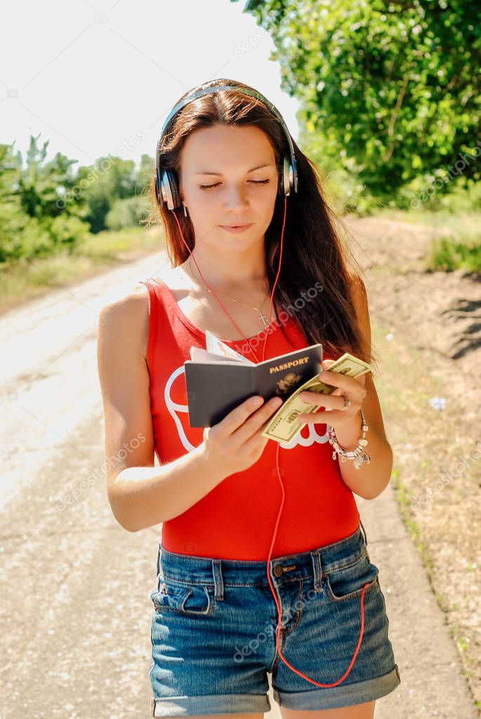 beautiful brunette woman with headphones on the road holding a passport with money.