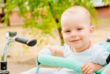 Küçük bebek arabası yeşil bahçesinde oturan oğlu.