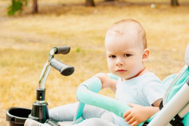Küçük bebek arabası yeşil bahçesinde oturan oğlu.