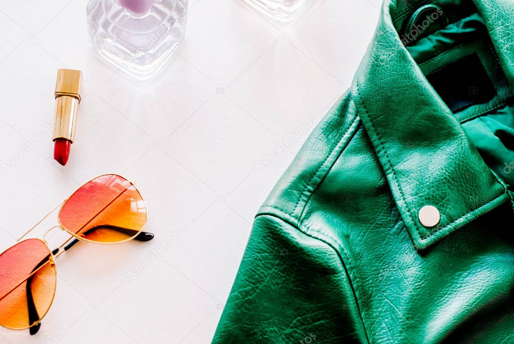 green leather jacket and sunglasses on white background. Alternative fashion set. Flat lay, top view.