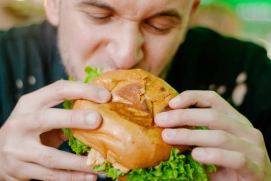 Bir restoranda hamburger yiyen adam, aç ve iyi bir ısırık içiyor. seçici odaklama