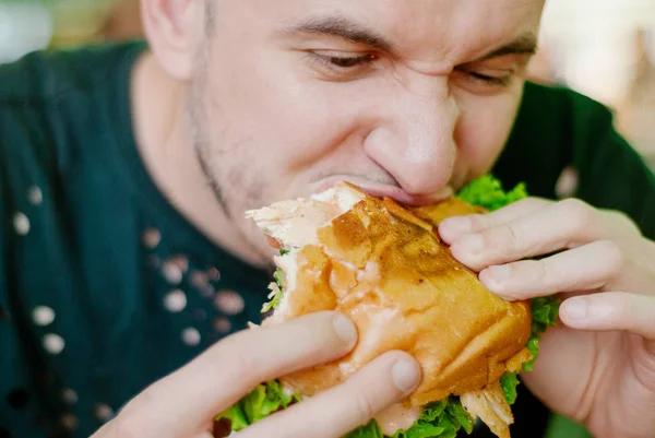Un uomo in un ristorante che mangia un hamburger, ha fame e ha un buon morso. focus selettivo — Foto Stock