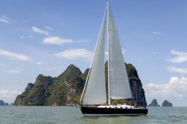 Phang Nga Körfezi 'nin turkuaz sularında ilerleyen bir yelkenli, parlak mavi gökyüzünün altındaki yüksek kireçtaşı kayalıklarıyla çevrili. Yelkenli maceraları için mükemmel koşullar..