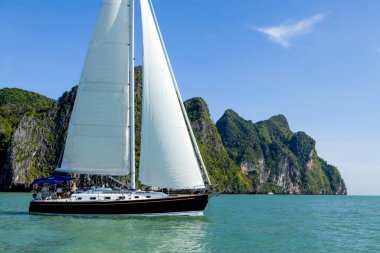 Phang Nga Körfezi 'nin turkuaz sularında ilerleyen bir yelkenli, parlak mavi gökyüzünün altındaki yüksek kireçtaşı kayalıklarıyla çevrili. Yelkenli maceraları için mükemmel koşullar..