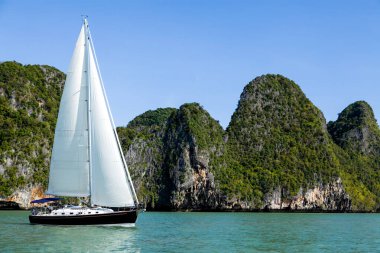 Phang Nga Körfezi 'nin turkuaz sularında ilerleyen bir yelkenli, parlak mavi gökyüzünün altındaki yüksek kireçtaşı kayalıklarıyla çevrili. Yelkenli maceraları için mükemmel koşullar..